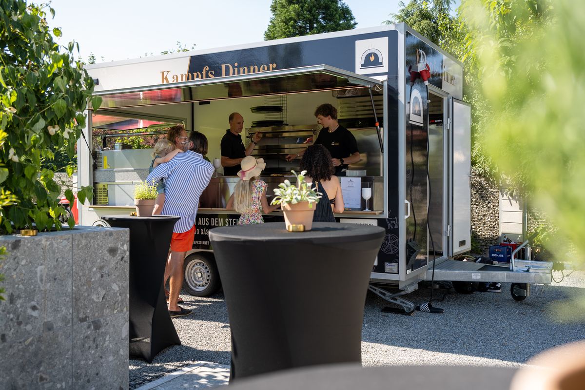 Der Pizza-Anhänger von Kampfs Dinner steht bei einem Gartenfest, Gäste warten an Stehtischen auf ihre Pizza