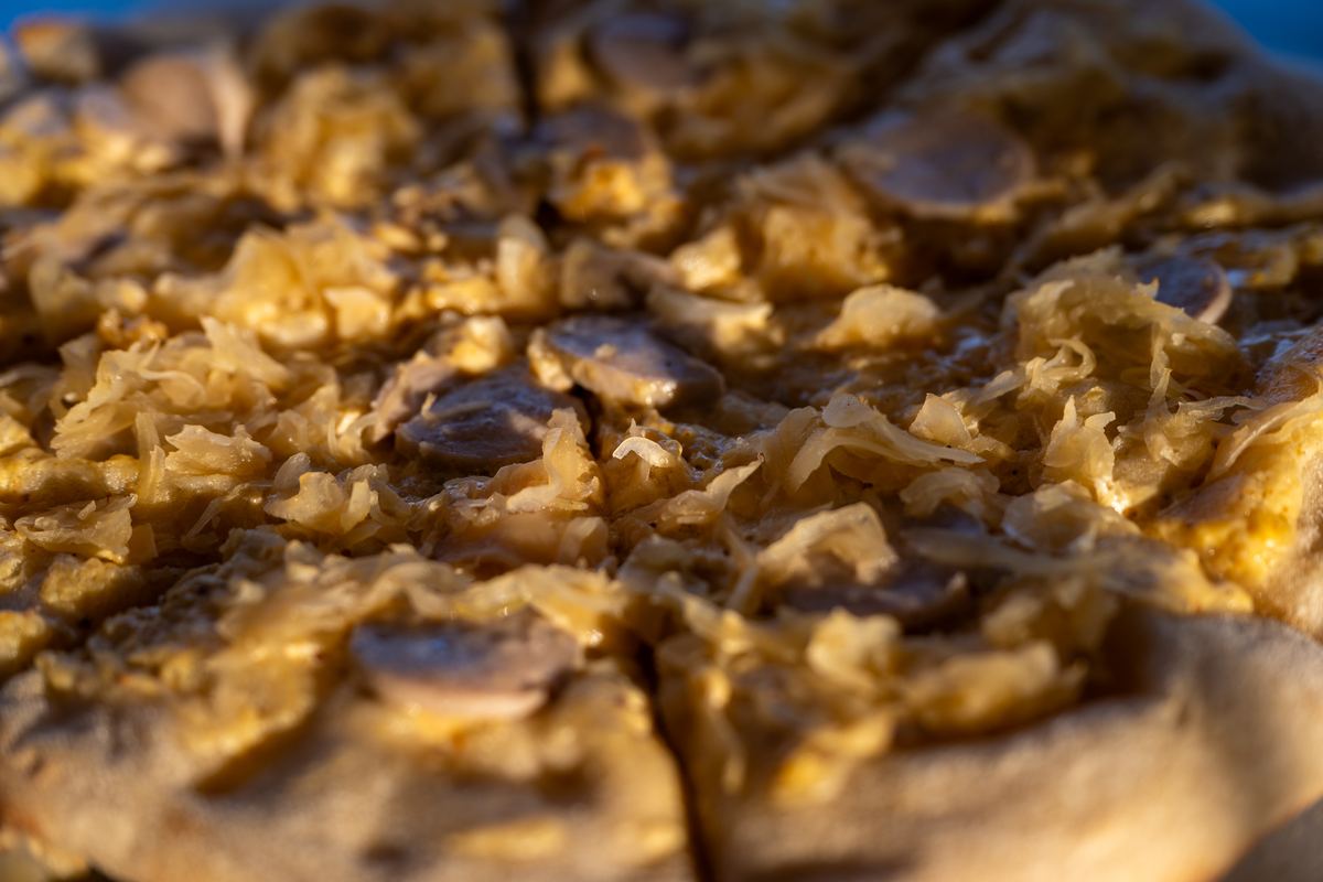 Nahaufnahme der Bayerischen Pizza: Sauerkraut und Weißwurstscheiben auf goldbraunem Pizzateig