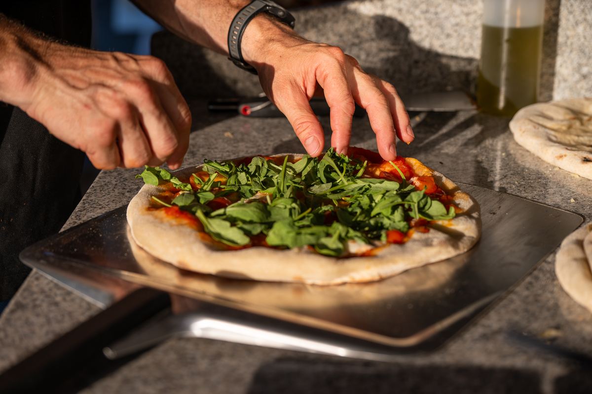 Alexander Kampf belegt eine Pizza mit Rucola, bevor sie in den Ofen kommt