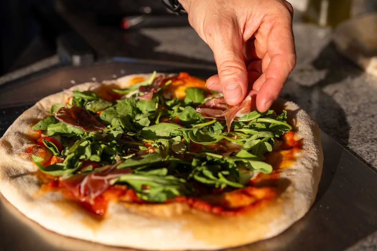 Fertige Pizza mit Rucola und Prosciutto auf dem Holzbrett im Abendlicht